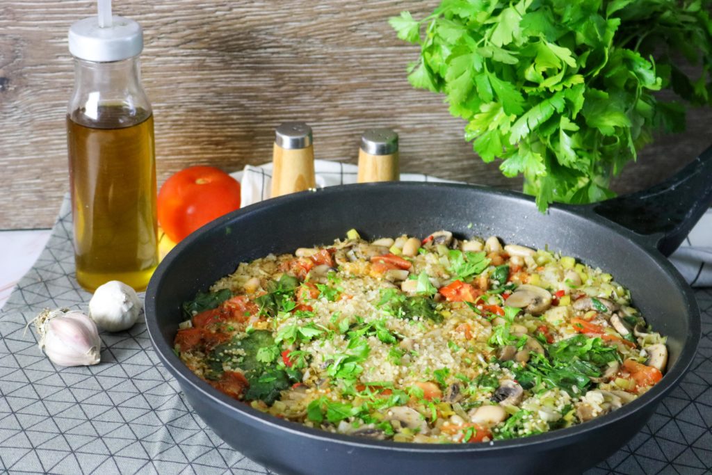 spinach, mushroom, and leek quinoa skillet with oil, garlic, tomatoes and seasoning surrounding it