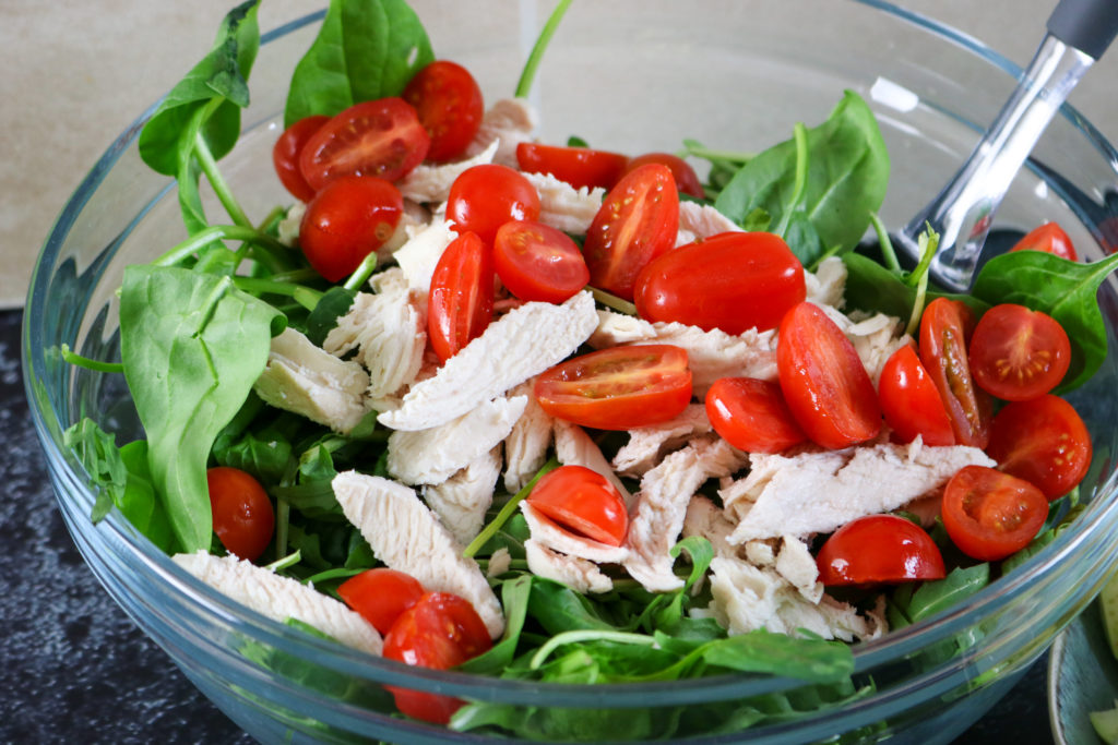 tomatoes, spinach and chicken in bowl, being mixed