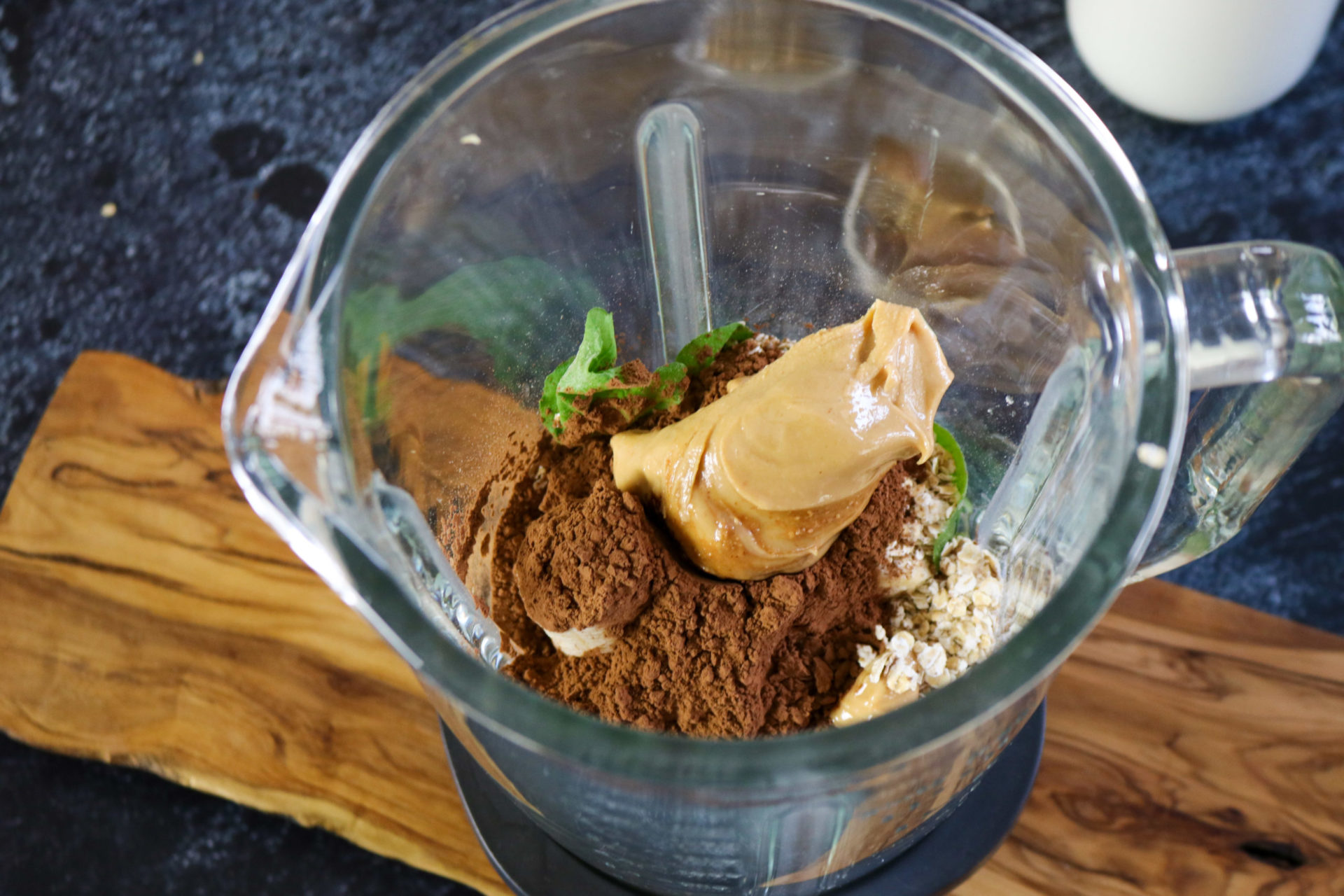 blender filled with peanut butter, cacao powder, oats and spinach